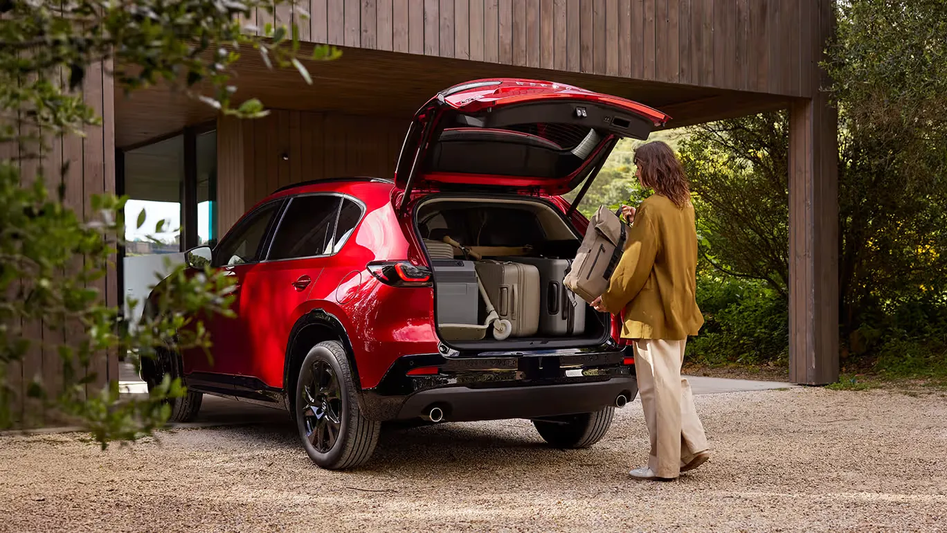 Mazda CX-5 piros SUV nyitott csomagtartóval, egy nő bőröndöt pakol az autóba egy modern ház előtt
