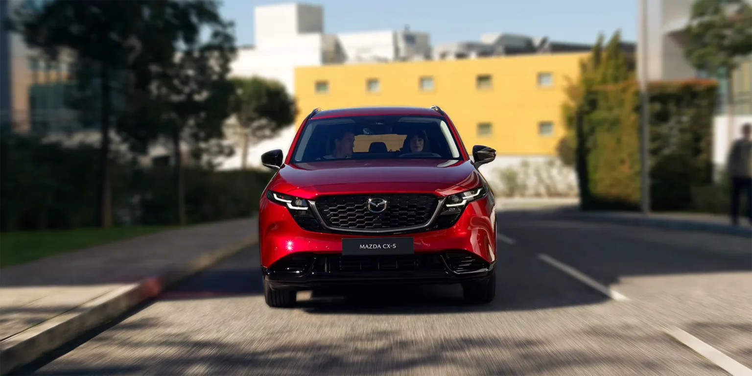 Mazda CX-5 piros SUV elölnézetből, városi úton haladva, két utassal az autóban