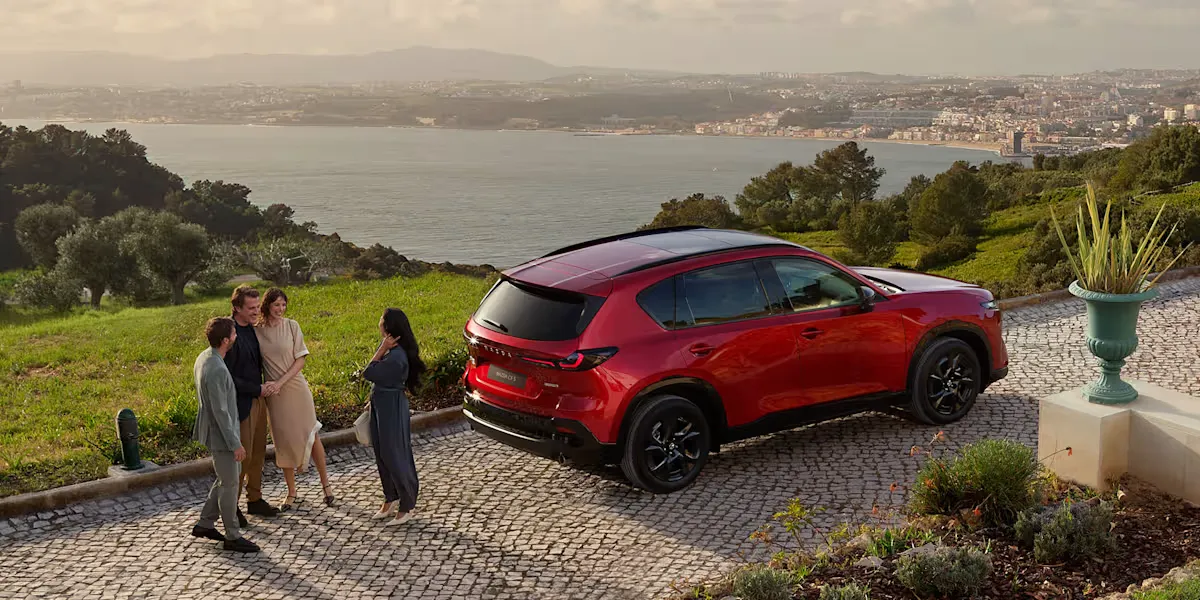 Mazda CX-5 piros SUV tengerparti panorámával, négy ember beszélget az autó mellett egy hegyvidéki úton